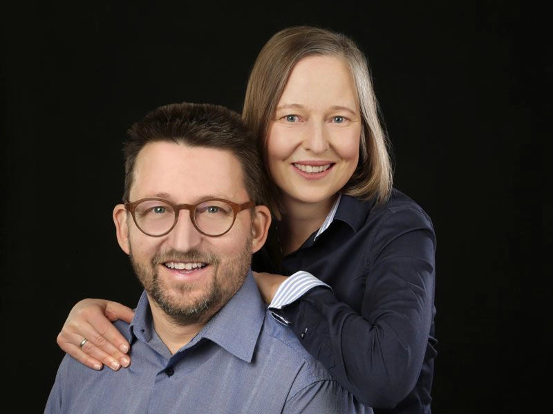 Zwei lächelnde Menschen, schwarze Hintergrund.